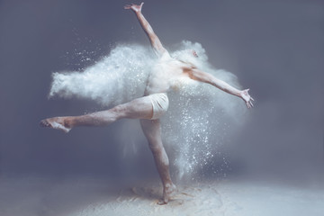 Dancing in flour concept. Naked muscle man dancer in dust / fog. Guy wearing white  shorts stretching his arms and putting his leg up on isolated background