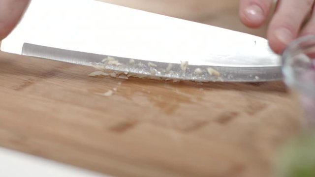 Tracking shot of chef mincing garlic clove with kitchen knife