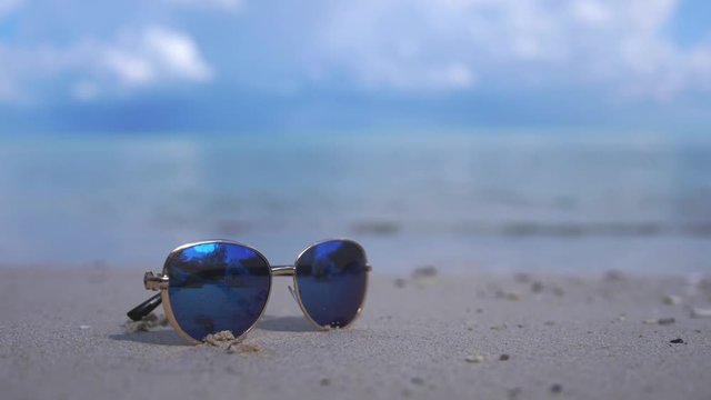 Travel and vacation concept. Blue sunglasses on a white ocean beach. Lazure turquoise sea in the background with copy space. 3840x2160