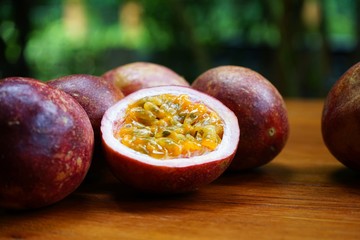 Fototapeta premium Group of passion fruit with half cut on wooden table with blur green garden background, copy space, healthy food concept