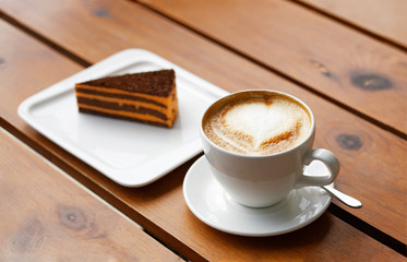 White cup of coffee cappuccino and piece of striped cake on a wooden table. Shallow focus.