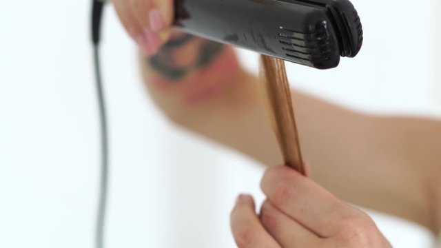 Hairstylist using hair tongs for curling hair for stylish hairstyle in beauty studio. Close up hairdresser using curling iron for stylish hairdo to long haired woman.