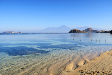 Fototapeta na wymiar Transparent ocean water with rocks and mountains at Sumbawa island beach, Indonesia
