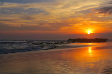 Fototapeta na wymiar Orange tropical sunset with reflection at Canggu beach, Bali, Indonesia