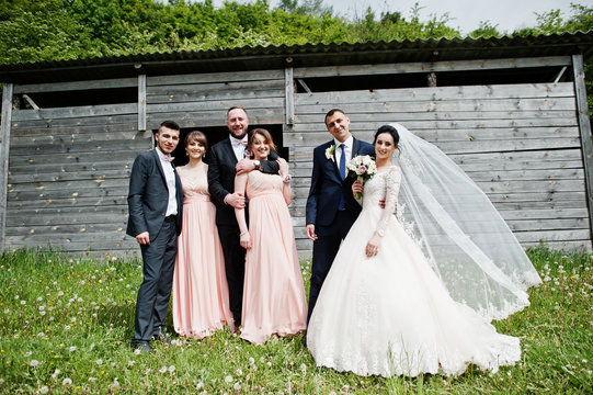 Bridesmaids with groomsmen and wedding couple having fun outdoors next to the old rustic wooden barn.
