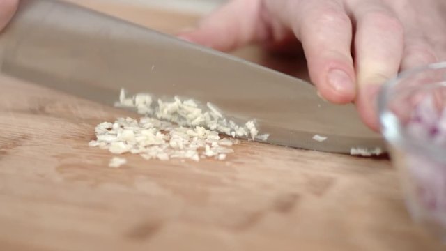 Tracking shot of chef mincing garlic clove with kitchen knife