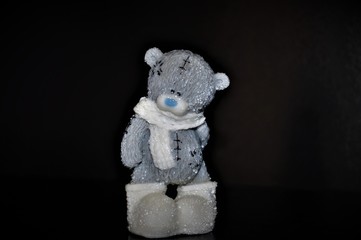 Gray teddy bear in a white scarf on a black background