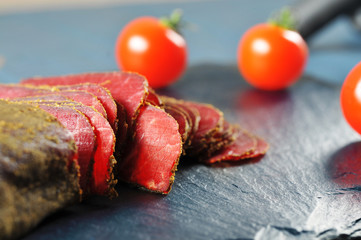 Sliced meat and tomatoes on the dark board with blurred background