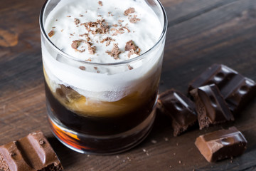 white russian cocktail with kahlua vodka and cream and chocolate pieces on wooden background