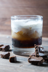 white russian cocktail with kahlua vodka and cream and chocolate pieces on wooden background