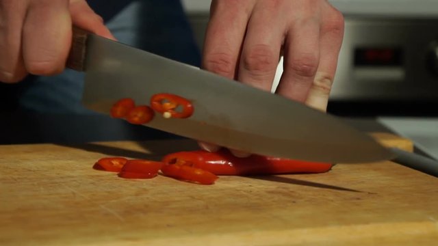 Slicing Red chili pepper. A man cuts pepper on a wooden Board