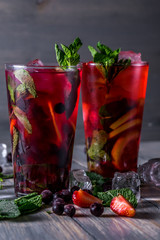 cocktail with  black currant, strawberry, mint, lemon, ice and some alcohol on wooden table background