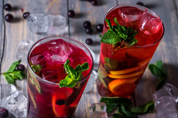 cocktail with  black currant, strawberry, mint, lemon, ice and some alcohol on wooden table background