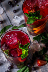 cocktail with  black currant, strawberry, mint, lemon, ice and some alcohol on wooden table background