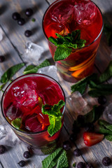 cocktail with  black currant, strawberry, mint, lemon, ice and some alcohol on wooden table background