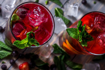 cocktail with  black currant, strawberry, mint, lemon, ice and some alcohol on wooden table...
