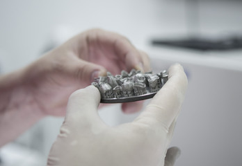 Man holds in hands object printed on metal 3d printer in laboratory. Dental crowns created in laser...