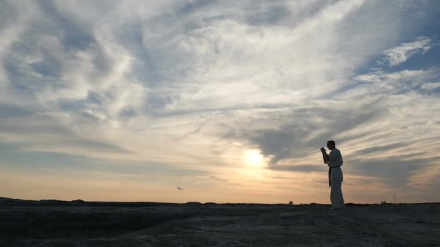 Karate sportsman kicks with his feet at sunset