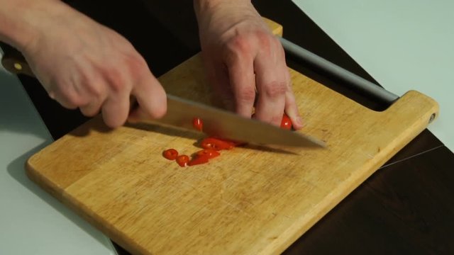 Slicing Red chili pepper. A man cuts pepper on a wooden Board
