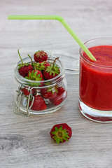 Healthy homemade strawberry smoothies in a glass with a straw for a cocktail and strawberries in a glass jar on a wooden board