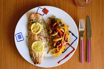 Primer plano de un plato de salmón con verduras visto desde arriba con cubiertos sobre una mesa de madera