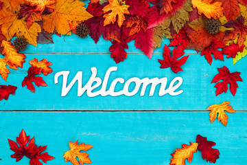 Welcome sign with colorful autumn leaves border hanging on rustic antique teal blue wood background; seasonal fall welcome sign