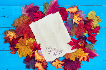Hope, Faith, Love on parchment paper with colorful autumn leaves border on rustic antique teal blue wood background; seasonal background with copy space