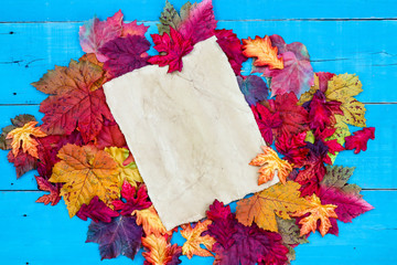 Blank parchment paper with colorful autumn leaves border on rustic antique teal blue wood background; seasonal background with copy space