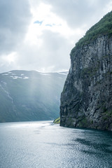 vertical picture massive geiranger fjord in norway seen from a cruise ship with light shining through the clouds