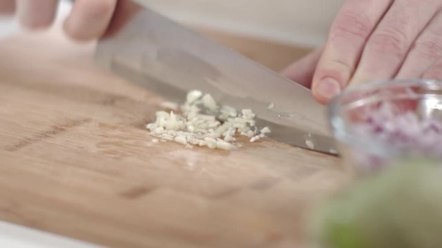 Slow-mo shot of chef mincing garlic clove with kitchen knife