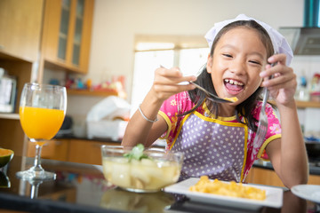 Little girl enjoy eating food with orange juice in kitchen