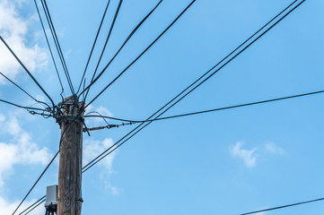 Old retro style wooden pole with many electric supply wires or cables against blue sky. Power line.