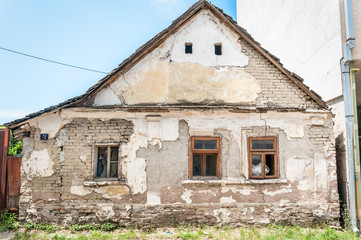 Fototapeta na wymiar Old rural abandoned house in the city with damaged collapsed plaster and bad foundation