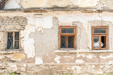 Fototapeta na wymiar Broken windows of old abandoned house with damaged plaster and bad foundation