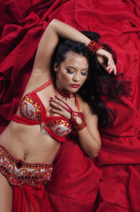 Top view of beautiful belly dancer posing and laying on floor against red backdrop