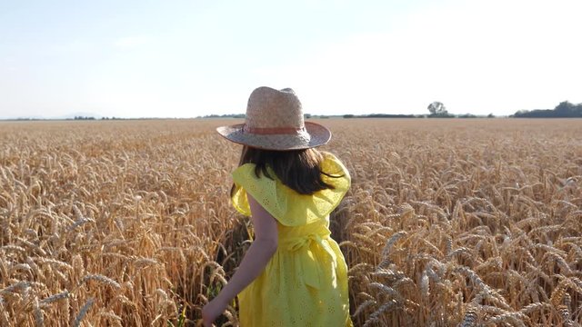 Kid girl in yellow dress enjoy walking and jumping in good mood on a wheat field in evening