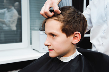 Obraz na płótnie Canvas Young handsome barber making haircut of cute boy in barbershop