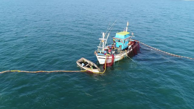 Installation of professional fishing gear in the sea. The fishermen unwind and set the network in a circle, on the small blue fishing boat and dinghy. Big birds near a boats. Aerial view.
