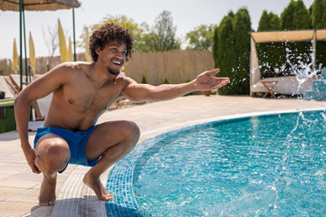 Beautiful young african american man splashing water at a pool