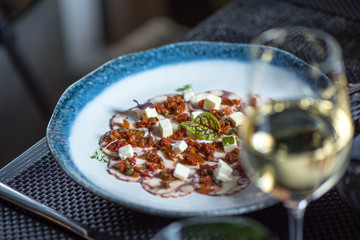 Carpaccio of octopus on blue plate with glass of white wine
