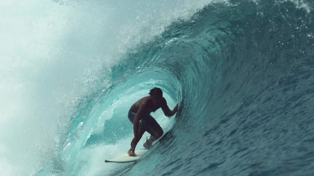 SLOW MOTION, CLOSE UP: Extreme sportsman having fun riding a beautiful barrel ocean wave. Breathtaking shot of active man on holiday surfing a perfect crystal clear hollow wave in Teahupoo, Tahiti.