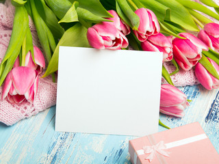 Pink tulip bouquet, gift box and balnk paper on blue wooden background, copy space.