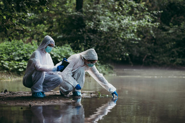 Two scientists in protective suits taking water samples from the river