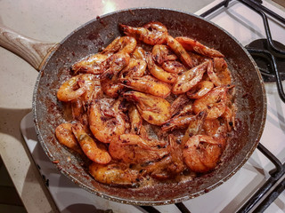 Giant orange shrimps with heads fried in oil in a frying pan on a gas stove
