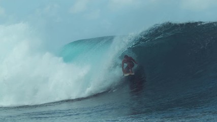 SLOW MOTION, CLOSE UP: Extreme male rider surfing in sunny Tahiti catches a big emerald colored tube wave. Man riding near a popular surf spot surfs along a perfect barrel wave rushing towards coast.