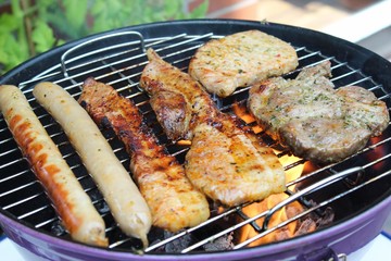 Bratwurst und mariniertes Fleisch (Nackensteak, Bauchfleisch) auf einem Holzkohle-Grill