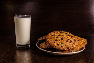 Plate with chocolate chip cookies and a glass of milk on a dark wooden table