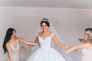 Happy bridesmaid hugging the bride in the bedroom in the morning. Before wedding ceremony. Bride...