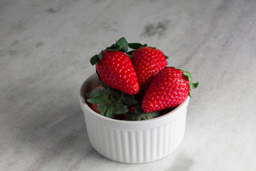 Heap fresh strawberries in the white porcelain bowl on the grey table background