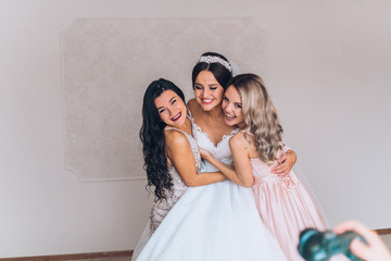 Happy bridesmaid hugging the bride in the bedroom in the morning. Before wedding ceremony. Bride preparing and wait groom. 